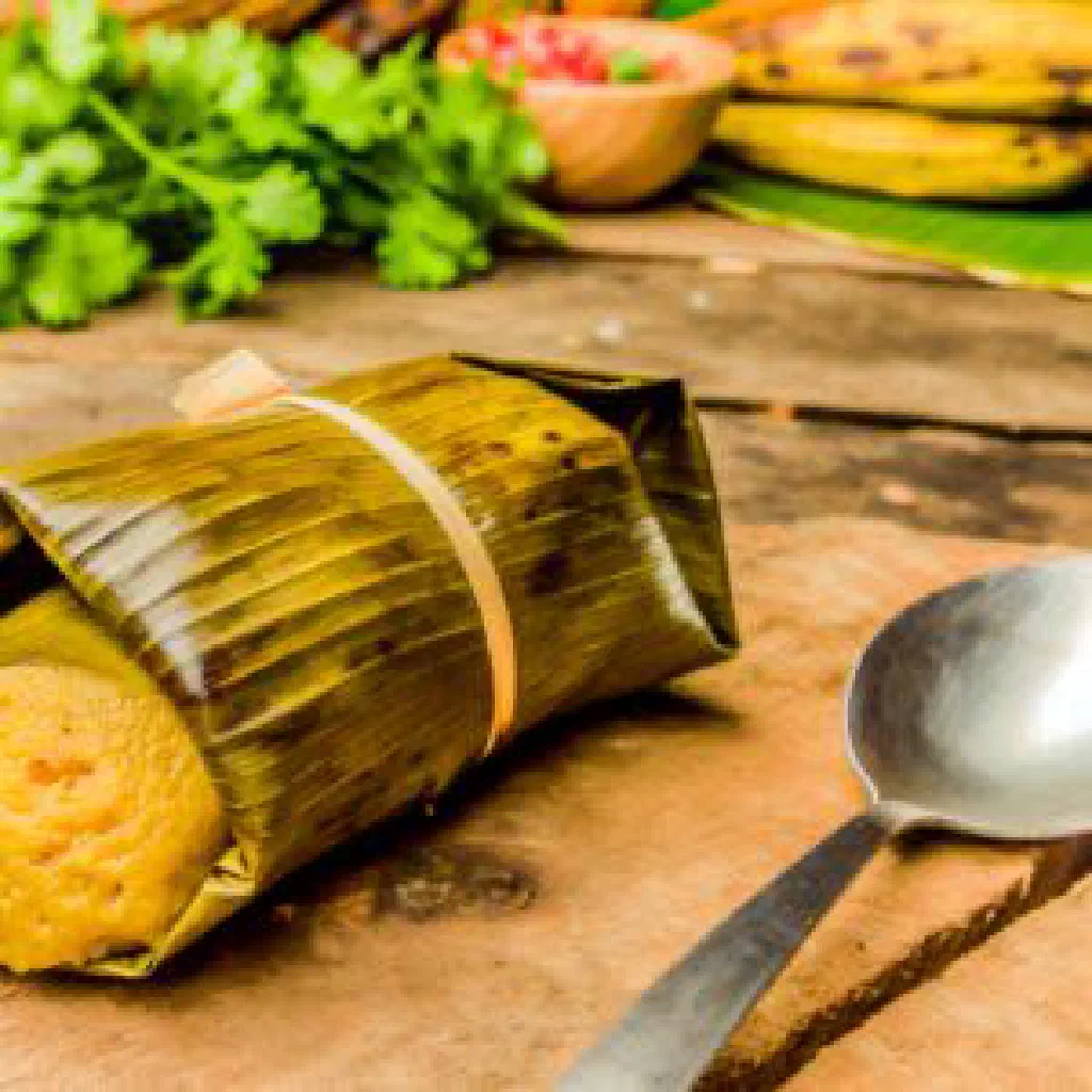 Steamed tamal de cambray wrapped in banana leaf, opened to show the corn masa and filling