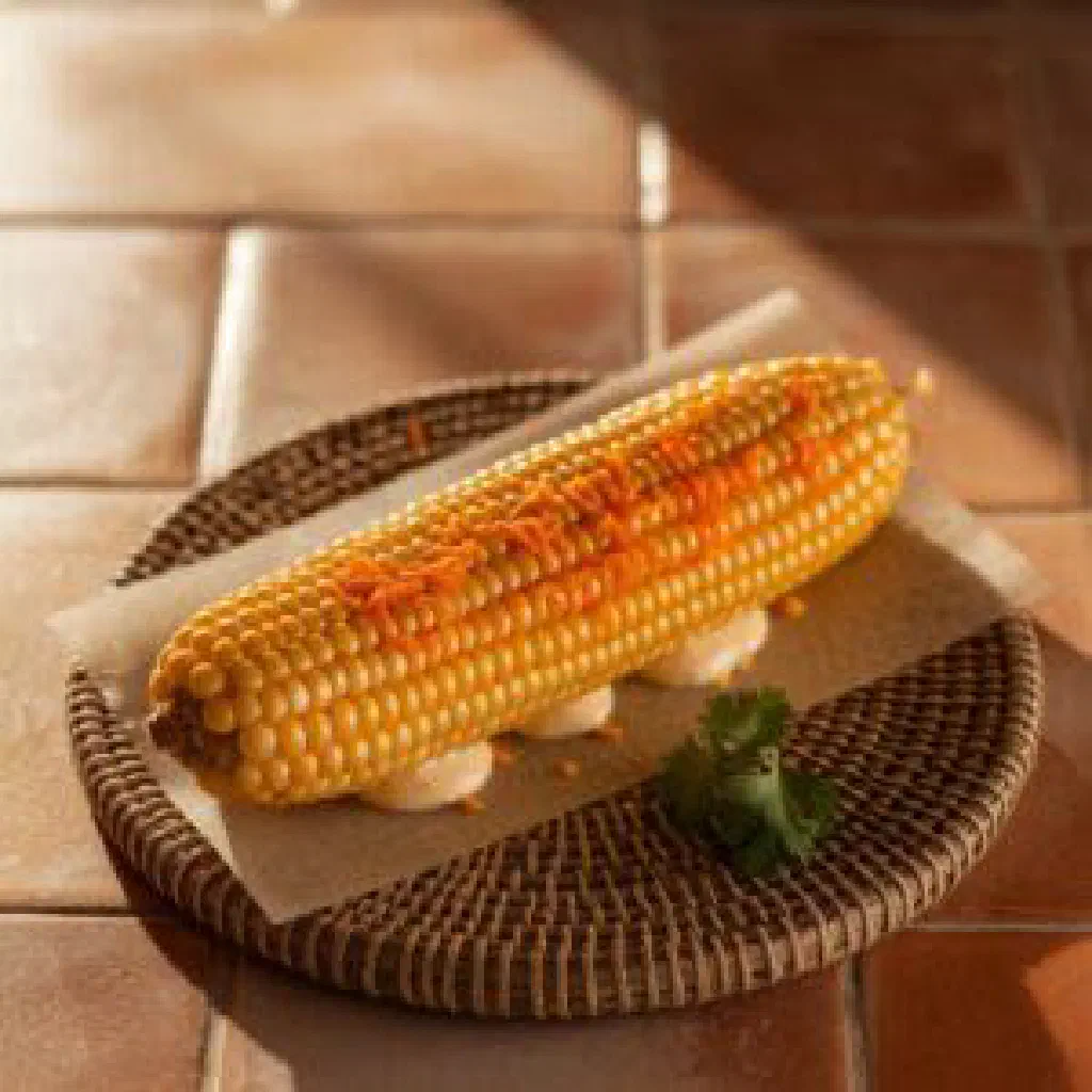 Boiled corn on the cob topped with mayonnaise and crumbled cheese