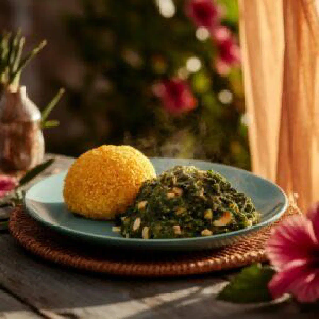 Creamy cornmeal coo coo served with spiced callaloo greens and lime
