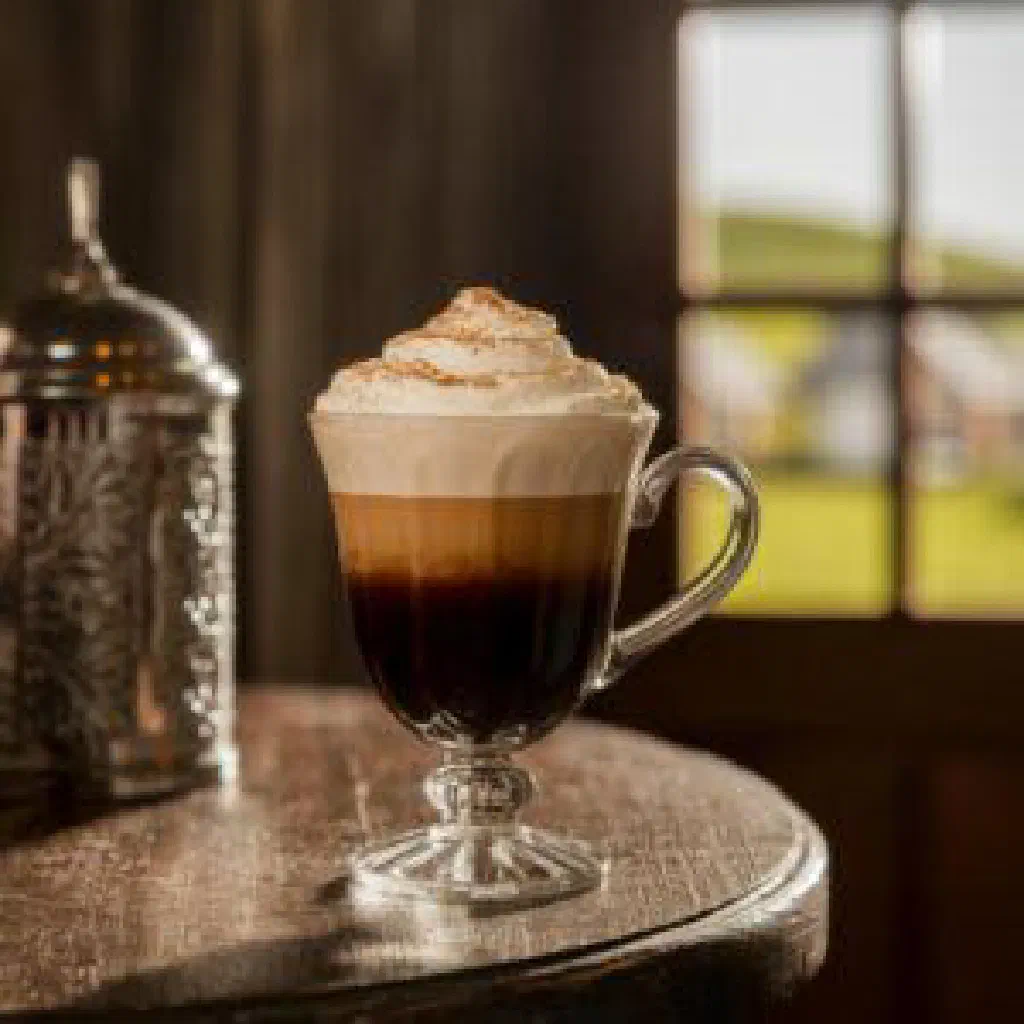 Non-alcoholic Irish coffee in a clear glass with a layer of cream and a dusting of cocoa
