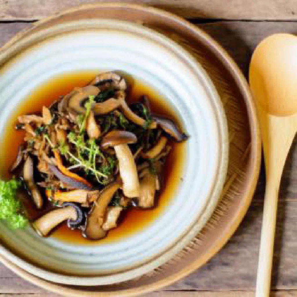 A clear Laotian mushroom soup garnished with fresh coriander and chilli