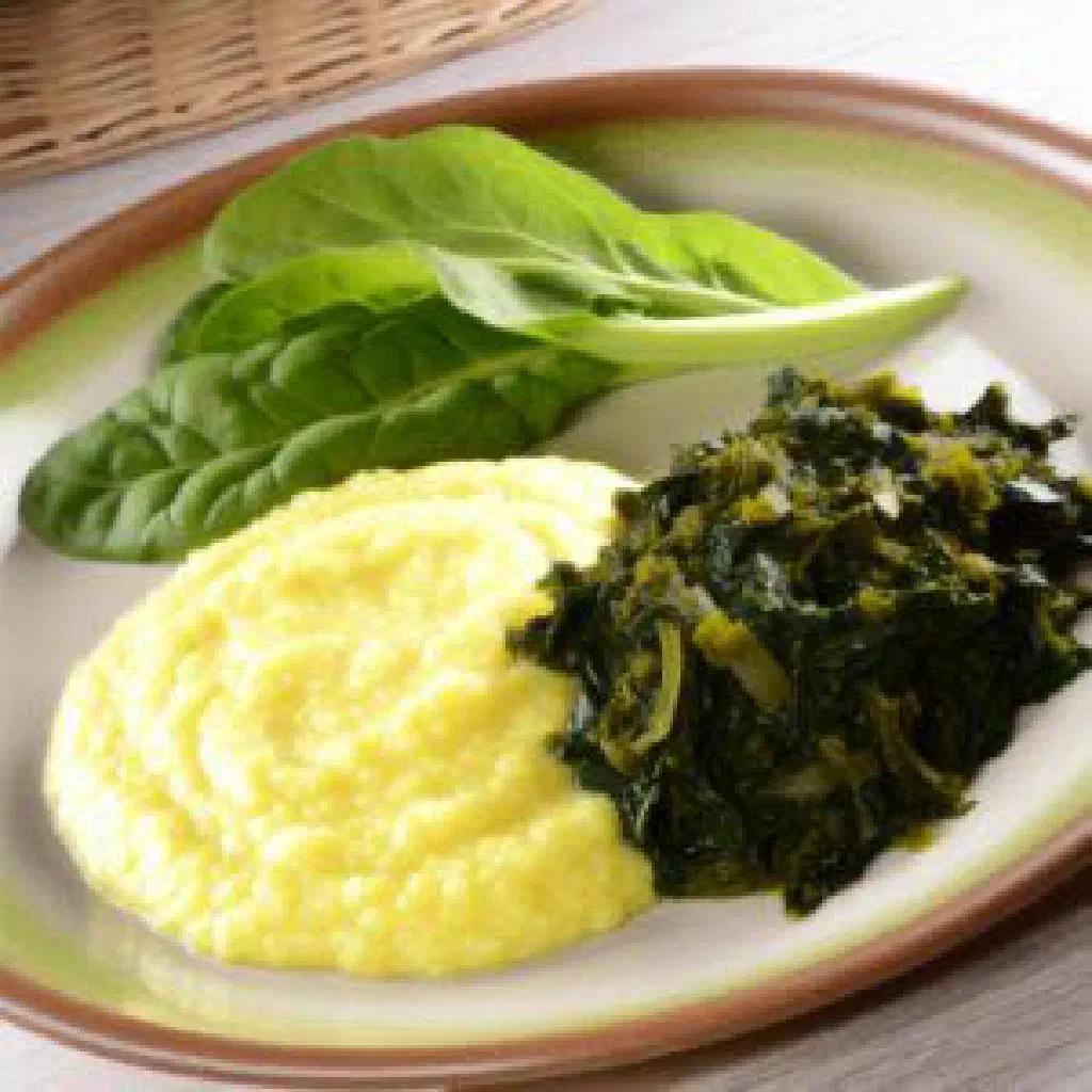 A bowl of soft white sima served with fresh cooked leafy greens