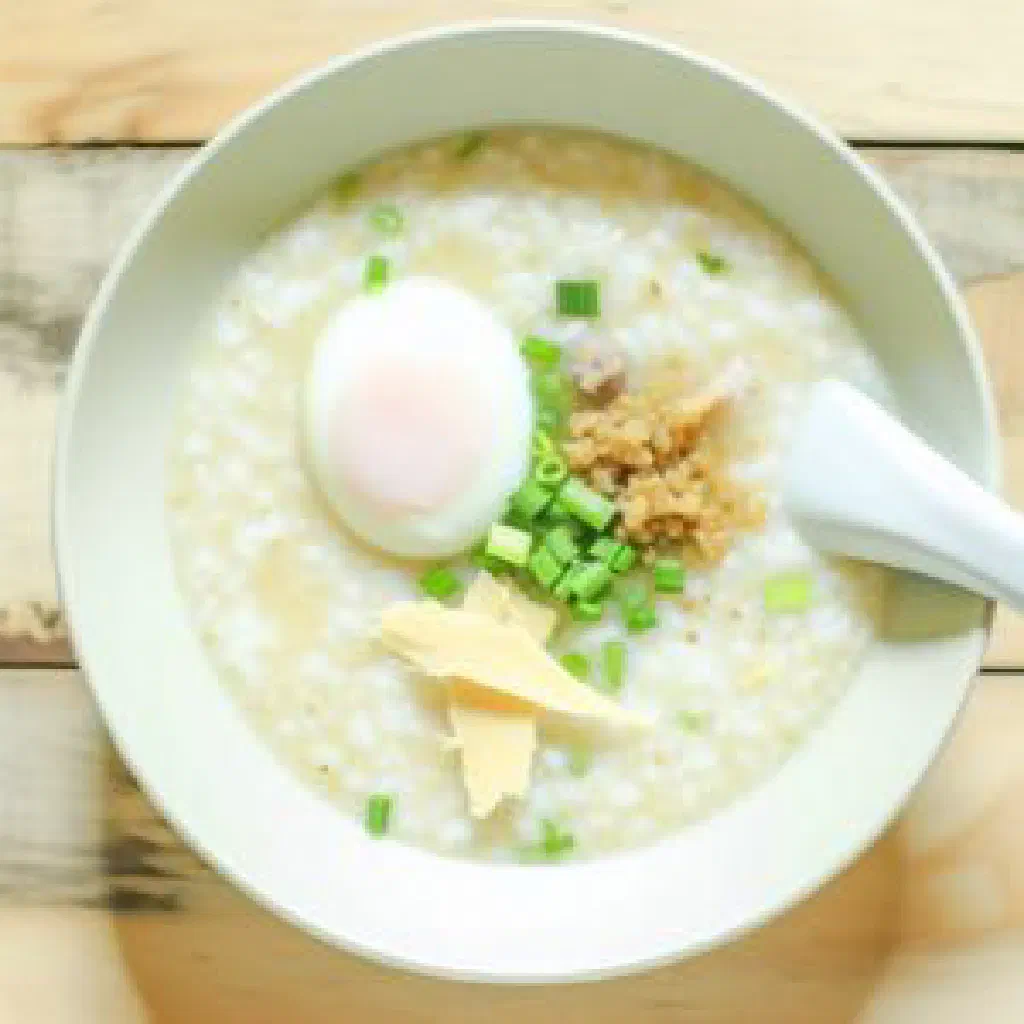 Bowl of Thai jok rice porridge topped with egg, spring onions and coriander