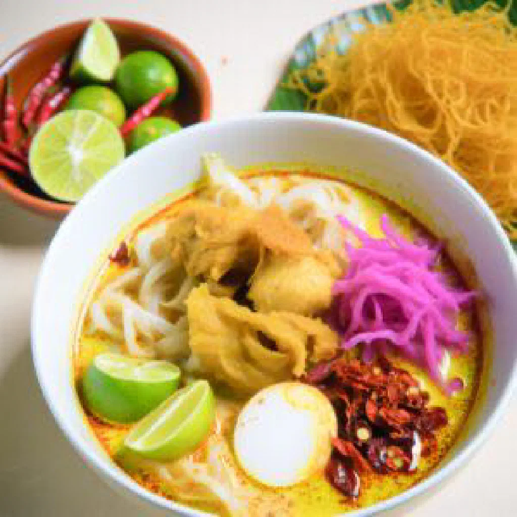 Bowl of khao soi gai with chicken in coconut curry broth topped with crispy noodles and lime
