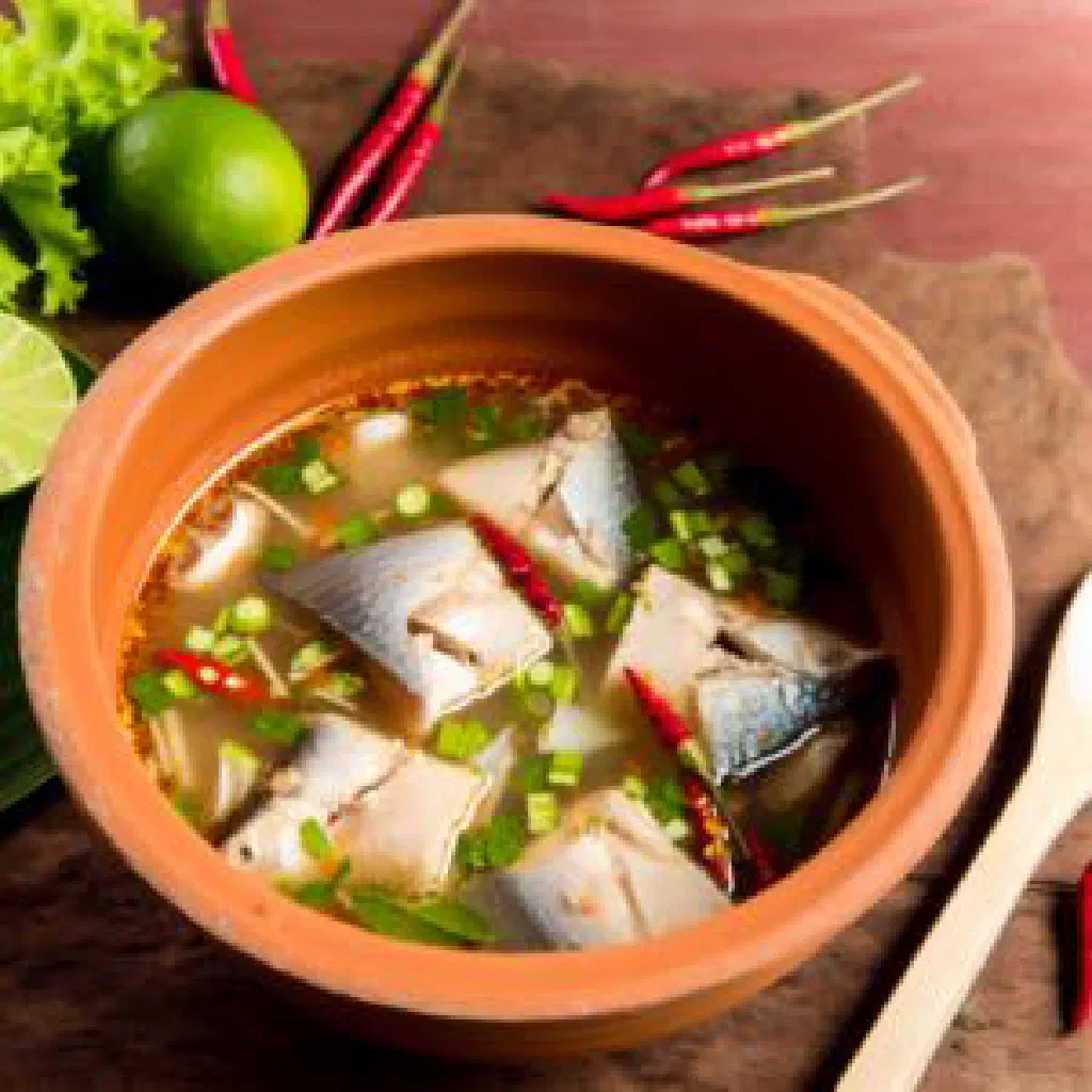 A steaming bowl of Tom Yam Pla fish soup garnished with fresh coriander and lime